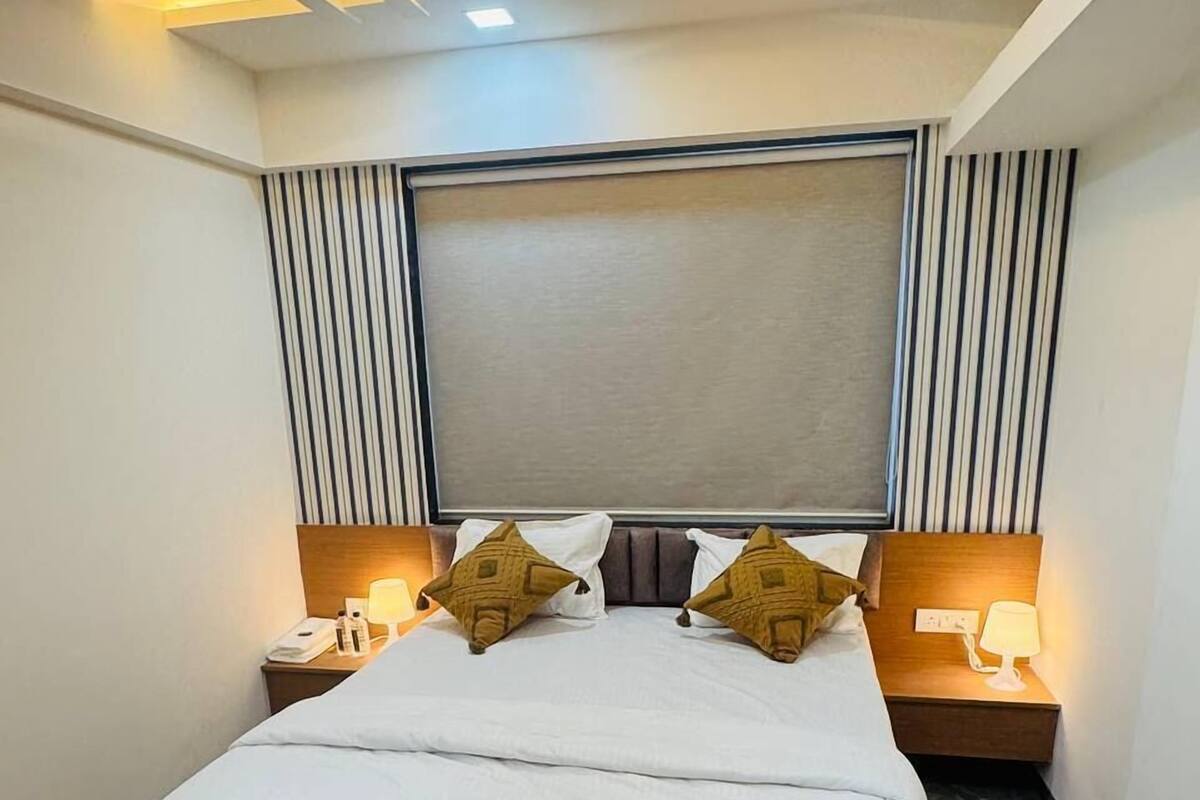 A hotel room with a large bed, two bedside tables with lamps, a headboard with vertical lines, and a ceiling light fixture.