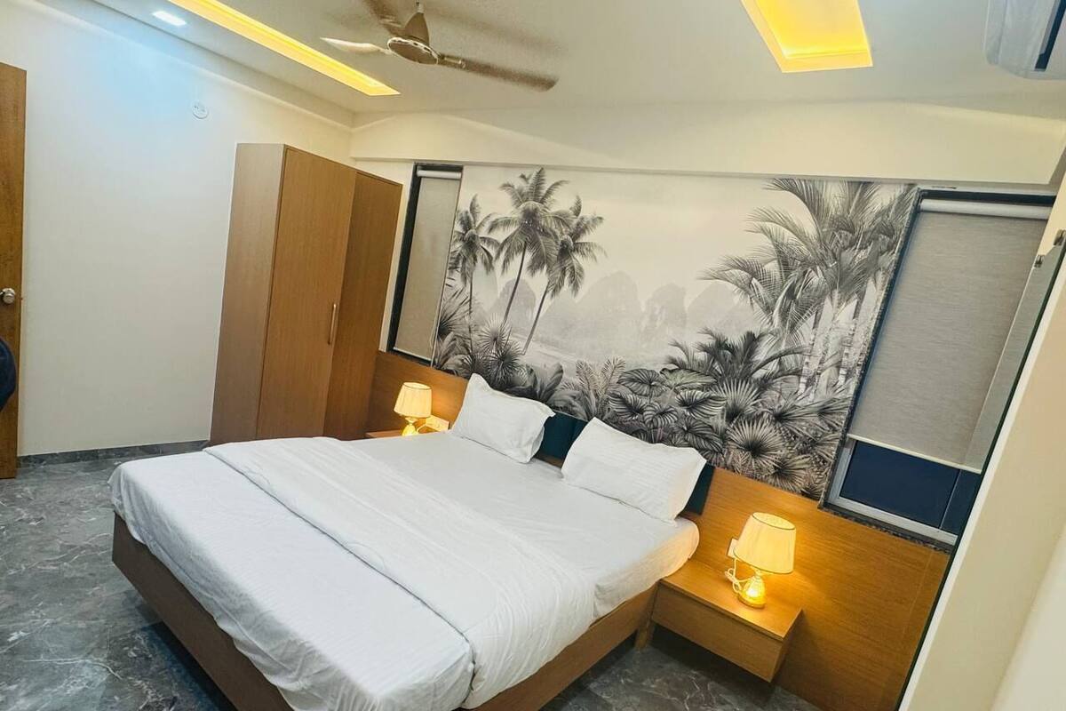 A bedroom with a bed, nightstands, a wardrobe, and a mural of palm trees.