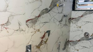 A bathroom with marble walls, a toilet, a shower, and a hand dryer. - Mighter Crest Studio Apartment (Nashik)