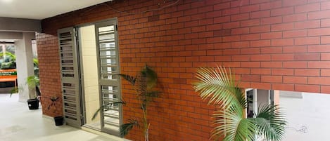 Amplio espacio interior con pared de ladrillo, puerta corredera de vidrio y varias plantas en macetas.