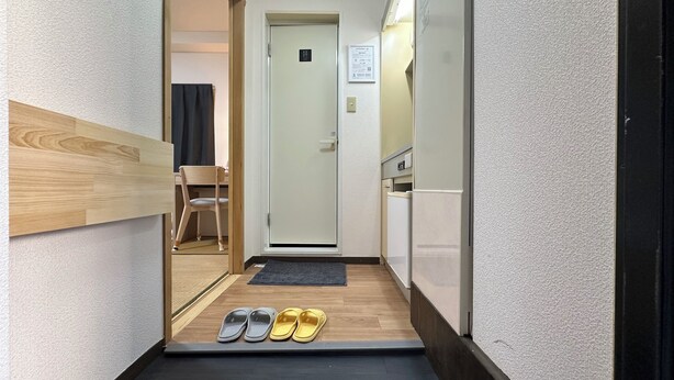 A narrow hallway with a wooden floor, a door with a sign, a chair, and a pair of slippers. - Cheap, 2-minute walk from the nearest station, 5 minutes to Namba by train, direct connection to Kansai International Airport, excellent access 【101 】. (大阪市)