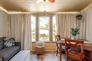 Un salon confortable avec un canapé, une table à manger et des chaises, une fenêtre avec des rideaux et un ventilateur de plafond.
