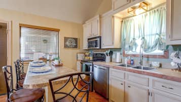 Une cuisine avec des meubles blancs, une cuisinière, un four à micro-ondes et un lave-vaisselle. On y trouve une table à manger avec des chaises et une fenêtre avec des stores.