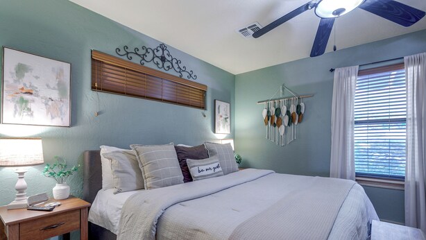 A bedroom with a bed, bedside table, lamp, wall art, and a ceiling fan. - 1/2 Mi to Lake Lawtonka: Mtn-View Haven! (Medicine Park)