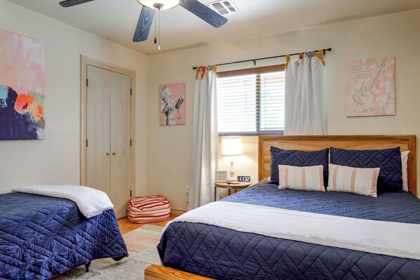 Ein Schlafzimmer mit zwei Betten, einem Fenster mit Vorhängen, einem Nachttisch mit Lampe und Bildern an den Wänden.