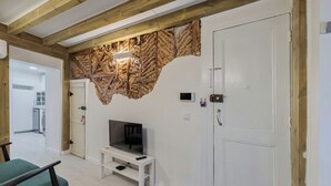 Une pièce avec un plafond en bois, une porte blanche, un téléviseur posé sur un meuble blanc et une chaise verte.