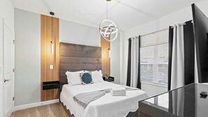Ein modernes Schlafzimmer mit einem großen Bett, einer Wandpaneinung aus Holz, einer Deckenleuchte und einem Fenster mit Jalousien.