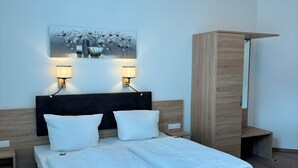 A modern hotel room with a large bed, two bedside lamps, a wooden wardrobe, and a wall-mounted artwork. - Pension Töpferhof (Tangermünde)