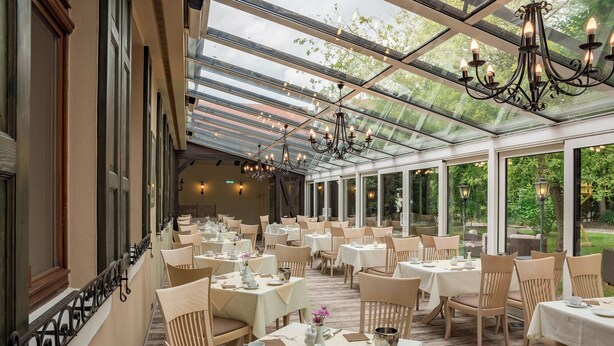 A restaurant with a glass ceiling, white tablecloths, and beige chairs. - Pension Töpferhof (Tangermünde)