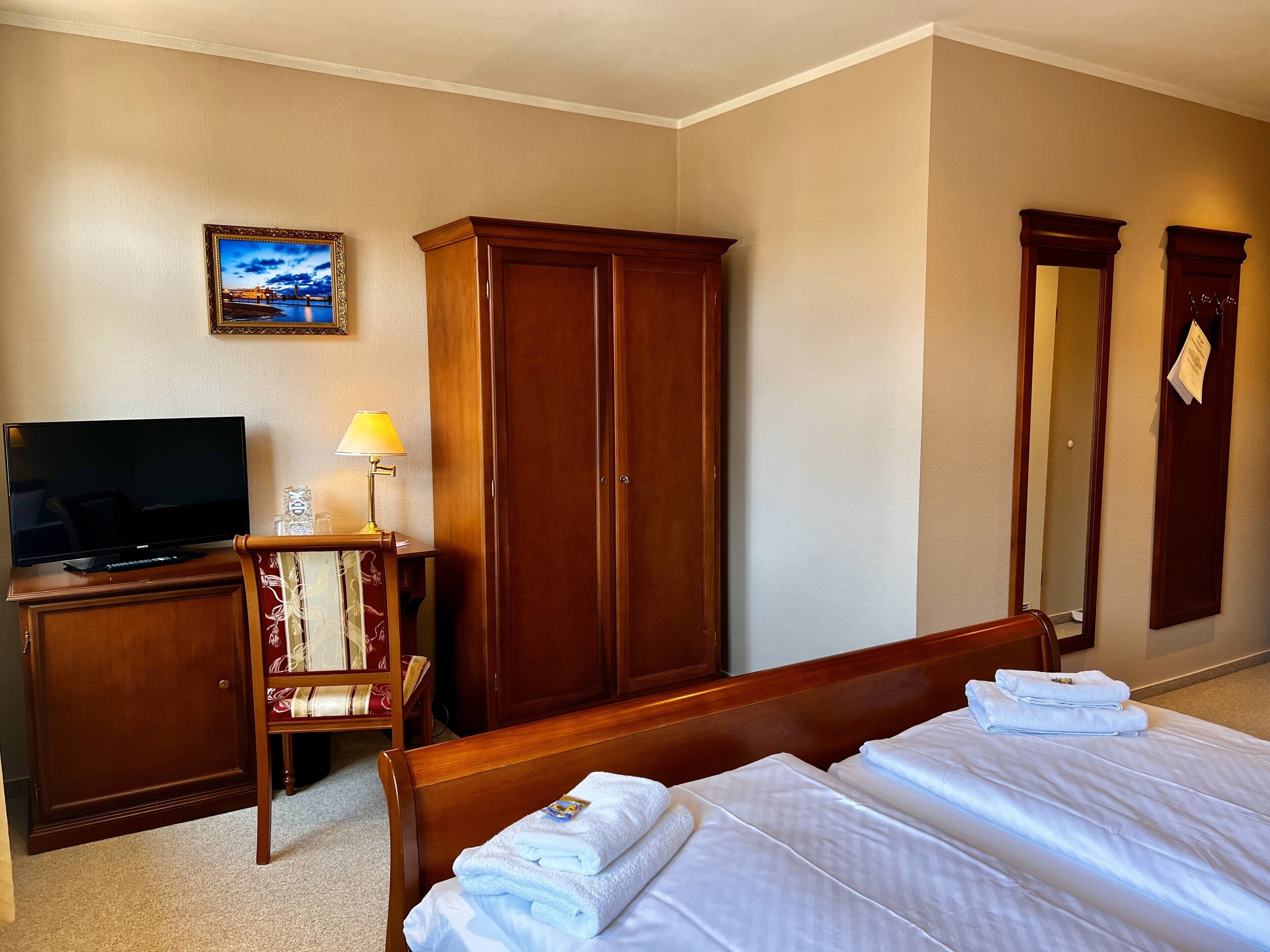 A hotel room with a bed, a TV, a wardrobe, and a desk with a lamp.