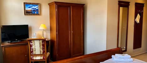 A hotel room with a bed, a TV, a wardrobe, and a desk with a lamp.