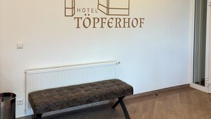 A hotel interior with a wall-mounted logo, a radiator, a bench, and a trash can. - Pension Töpferhof (Tangermünde)