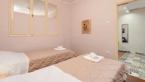 Ein Zimmer mit zwei Betten, einem großen Fenster, einem Spiegel und einer kleinen Pflanze an der Wand.