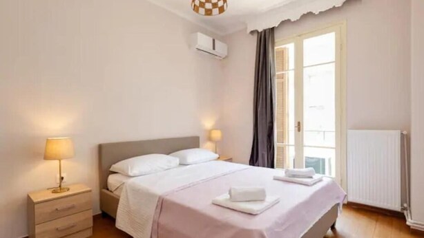 Ein Schlafzimmer mit Bett, Nachttisch, Lampe und Fenster mit Vorhängen.