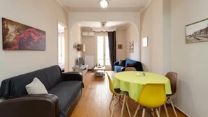 Ein Wohnzimmer mit einer Couch, einem Esstisch mit Stühlen, einem Fernseher und Kunstwerken an den Wänden.