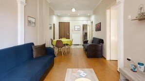 Ein Wohnzimmer mit einem blauen Sofa, einem Couchtisch und einem Essbereich mit Tisch und Stühlen.