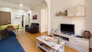 Ein modernes Wohnzimmer mit Sofa, Fernseher und Essbereich mit Tisch und Stühlen.