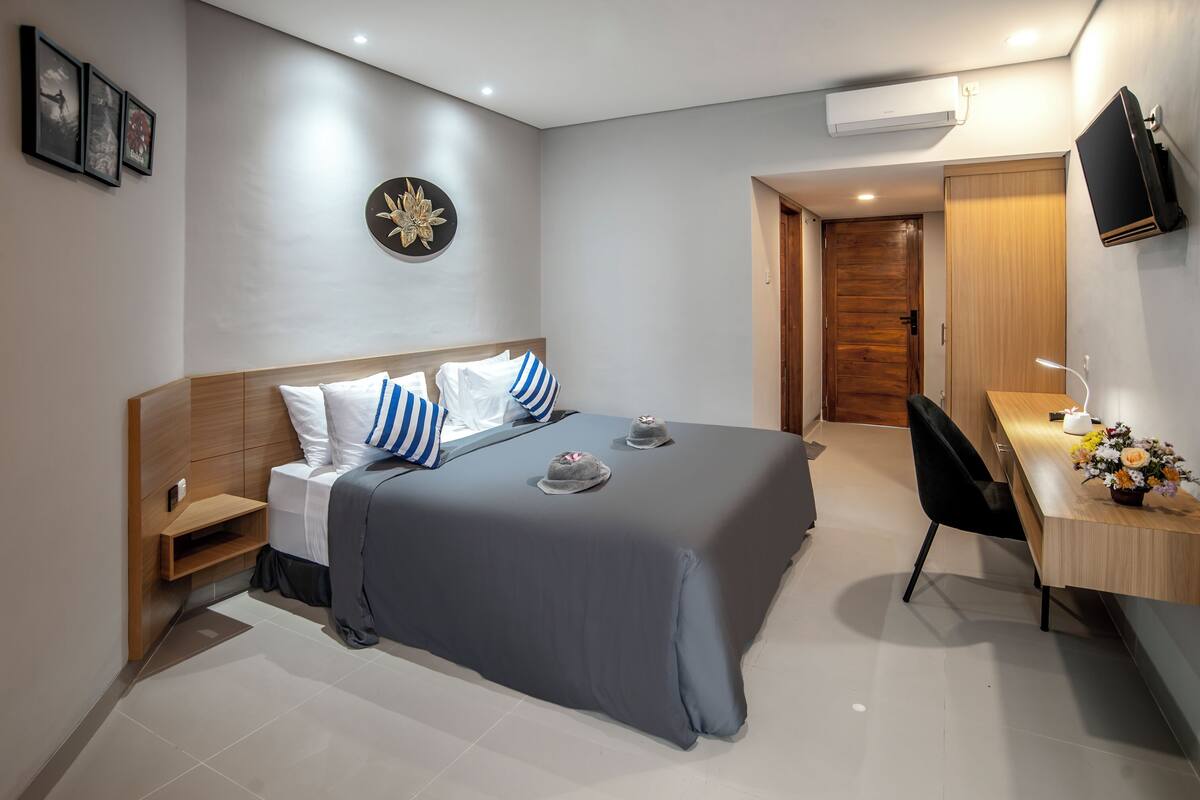 A modern hotel room with a large bed, bedside tables, a desk, and a TV.