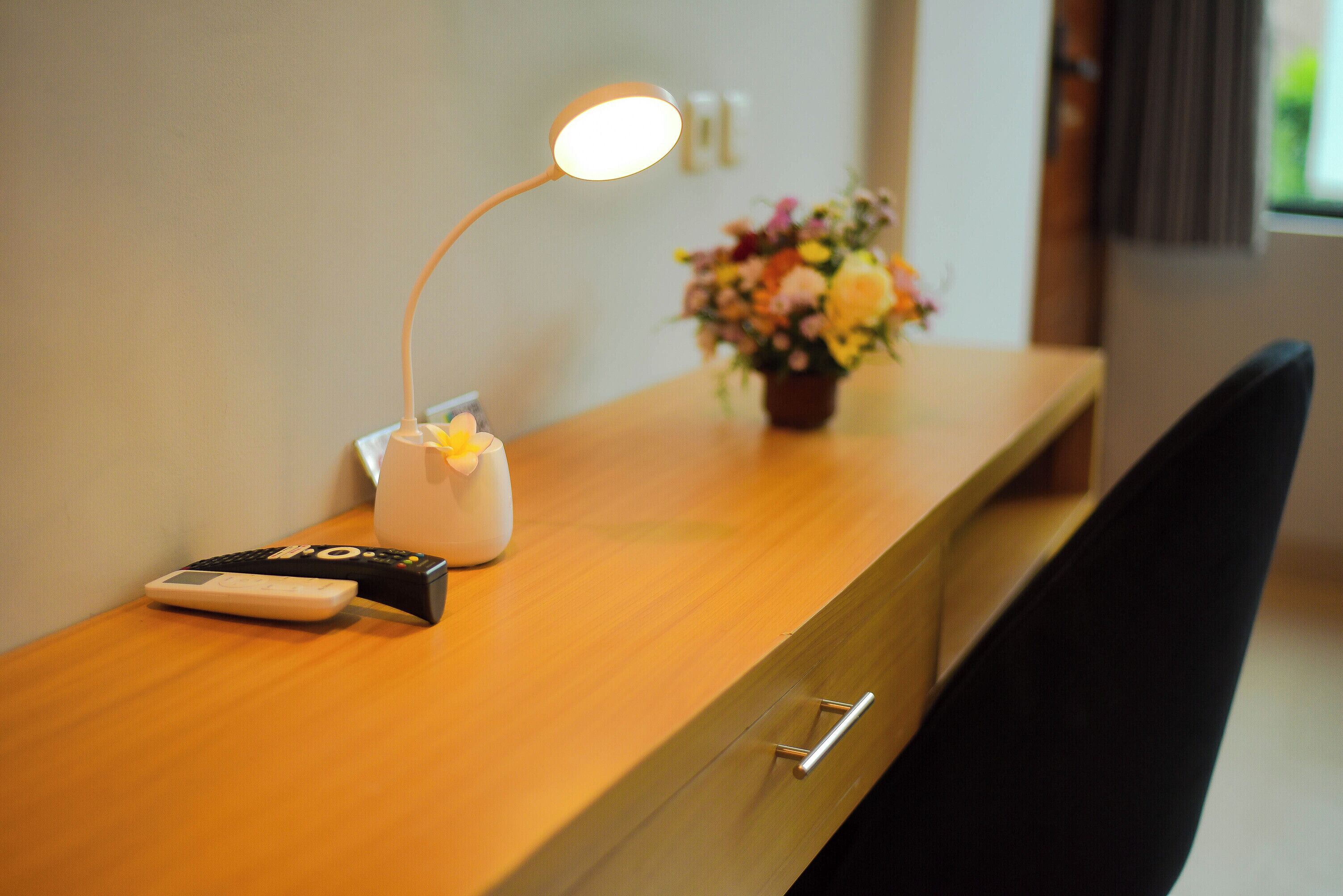 Una scrivania in legno con un telecomando, una lampada e un vaso con fiori.