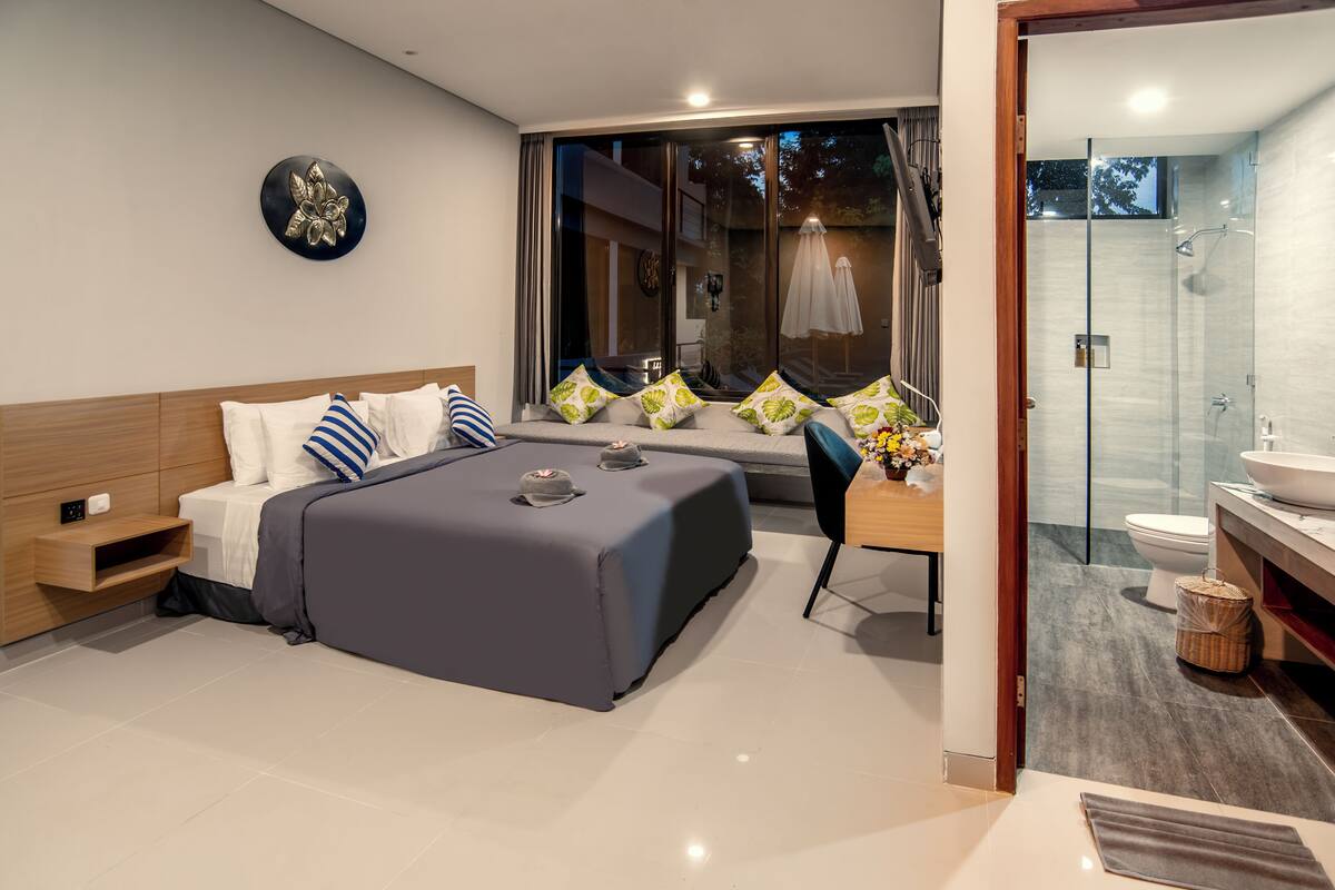 A modern bedroom with a large bed, a desk, and a shower area.