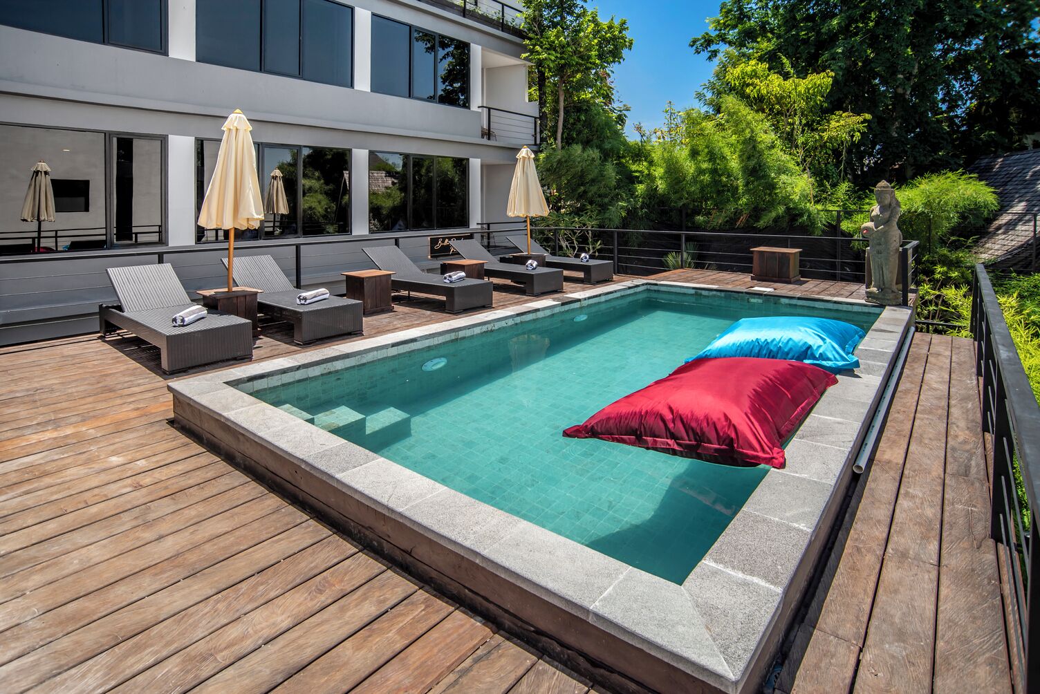 A modern outdoor swimming pool with lounge chairs and umbrellas, surrounded by a wooden deck and lush greenery.