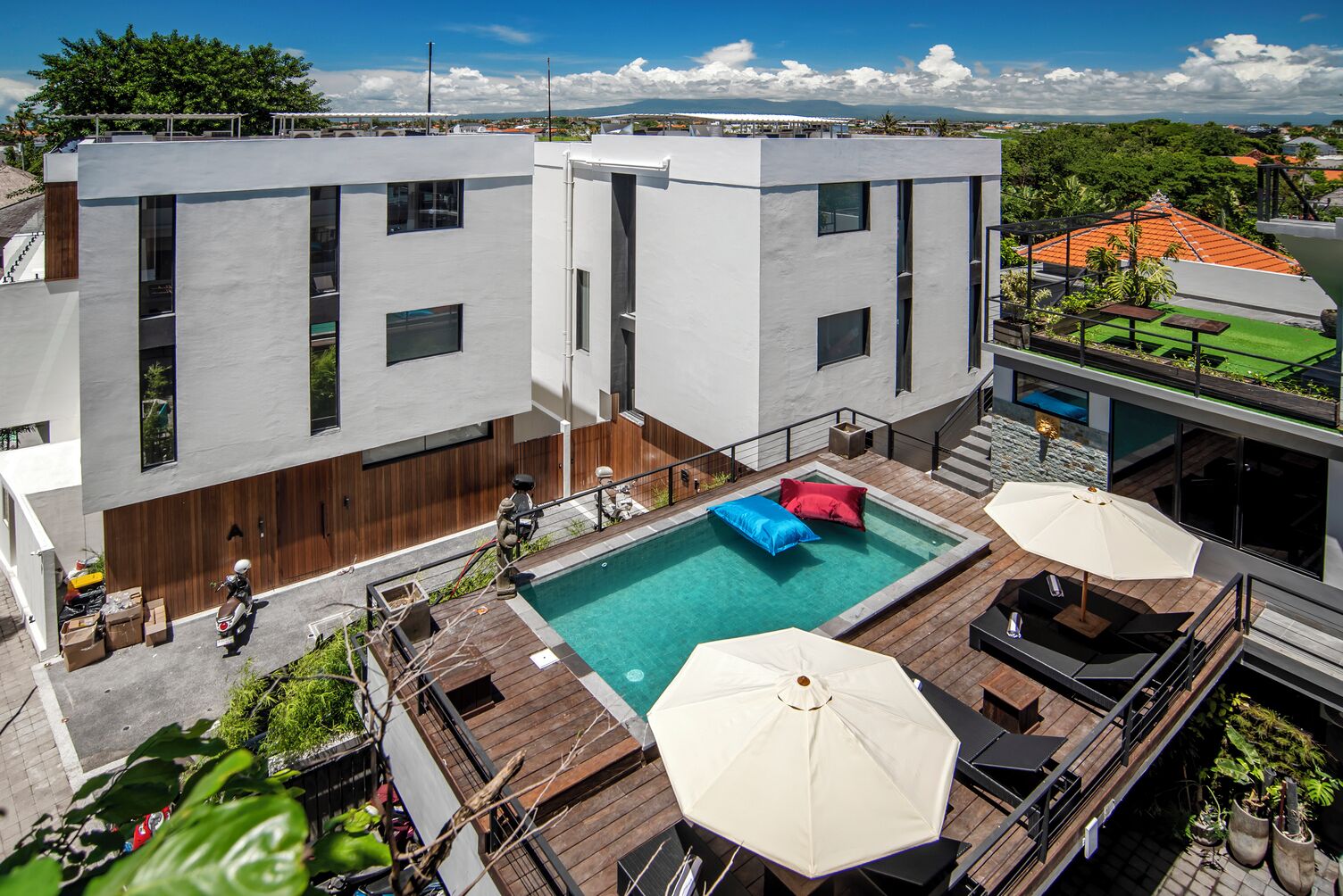 A modern building with a rooftop pool area, including a small pool, lounge chairs, and umbrellas.