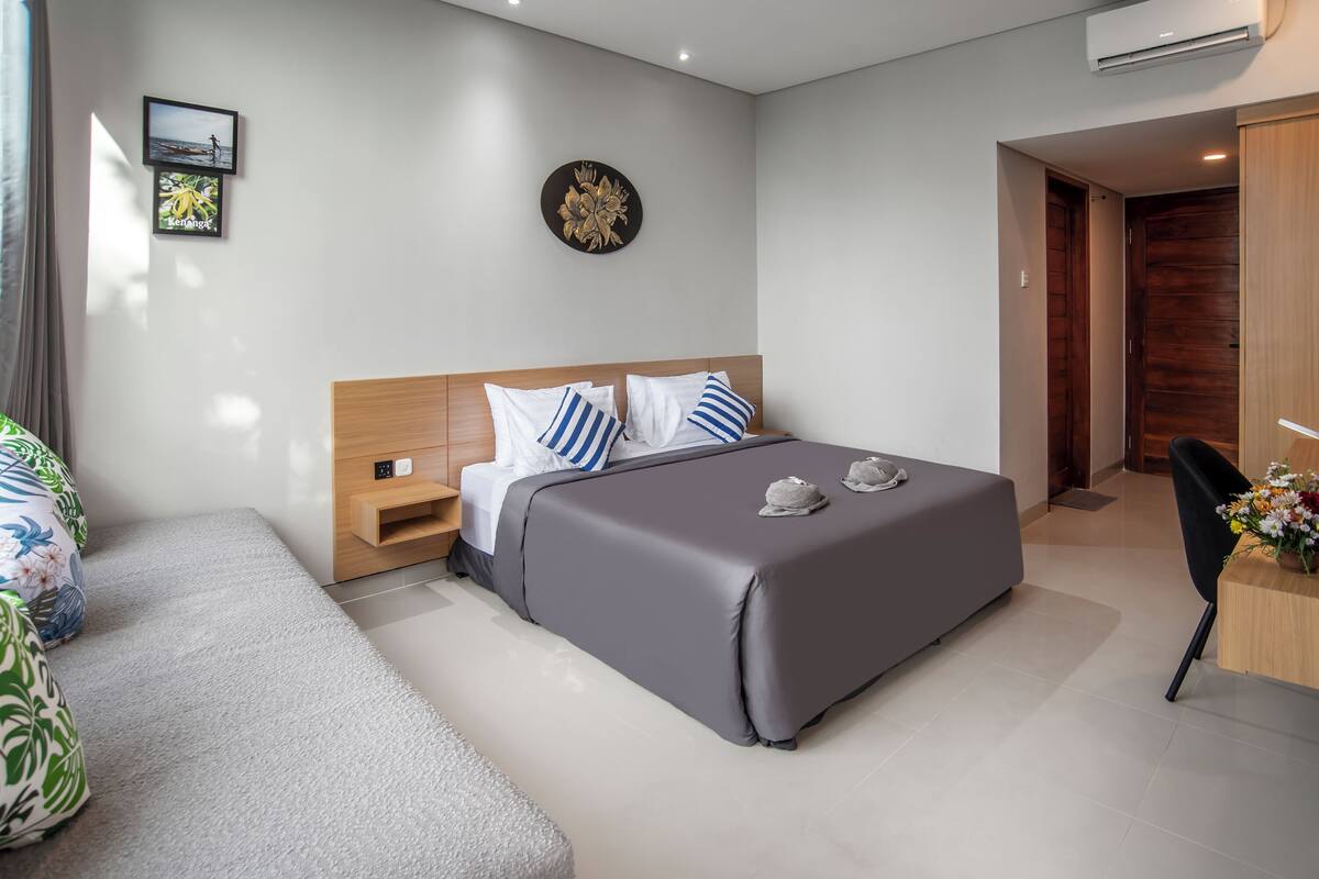 A modern hotel room with a large bed, a wooden headboard, and a desk with a chair.