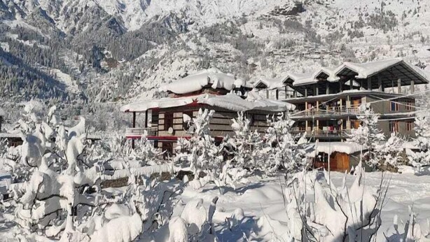 Un paysage de montagne enneigé, avec un hôtel composé de plusieurs bâtiments et une piste de ski en arrière-plan.