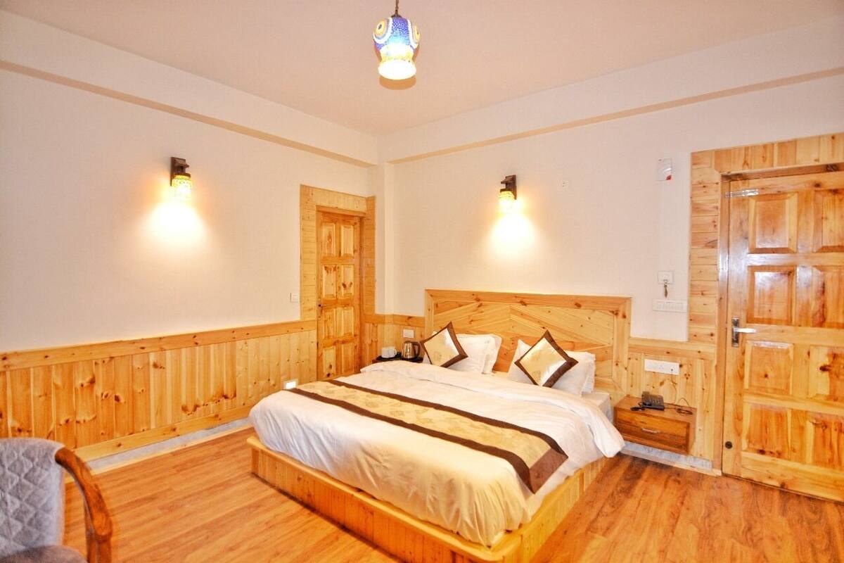 A wooden-paneled bedroom with a large bed, two wall-mounted lights, and a wooden wardrobe.