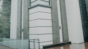 A modern building with a symmetrical facade, featuring a central vertical window and flanked by two sets of columns. - Ratu homestay (Bandar Lampung)