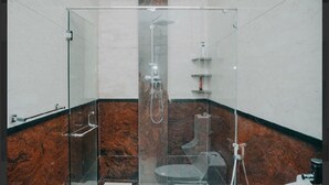 A glass-enclosed shower area with a marble floor, a handheld showerhead, and a wall-mounted faucet. - Ratu homestay (Bandar Lampung)