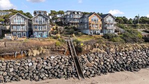 Un área residencial costera con varias casas, una orilla rocosa y un paseo de madera que lleva a la playa.