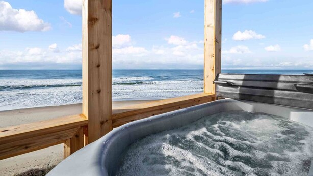 Una terraza de madera con un jacuzzi que da a una playa y al océano.