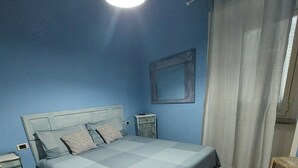 A bedroom with a bed, nightstands, a wooden floor, and a window with curtains. - La casina di Silverio (Rio Marina)