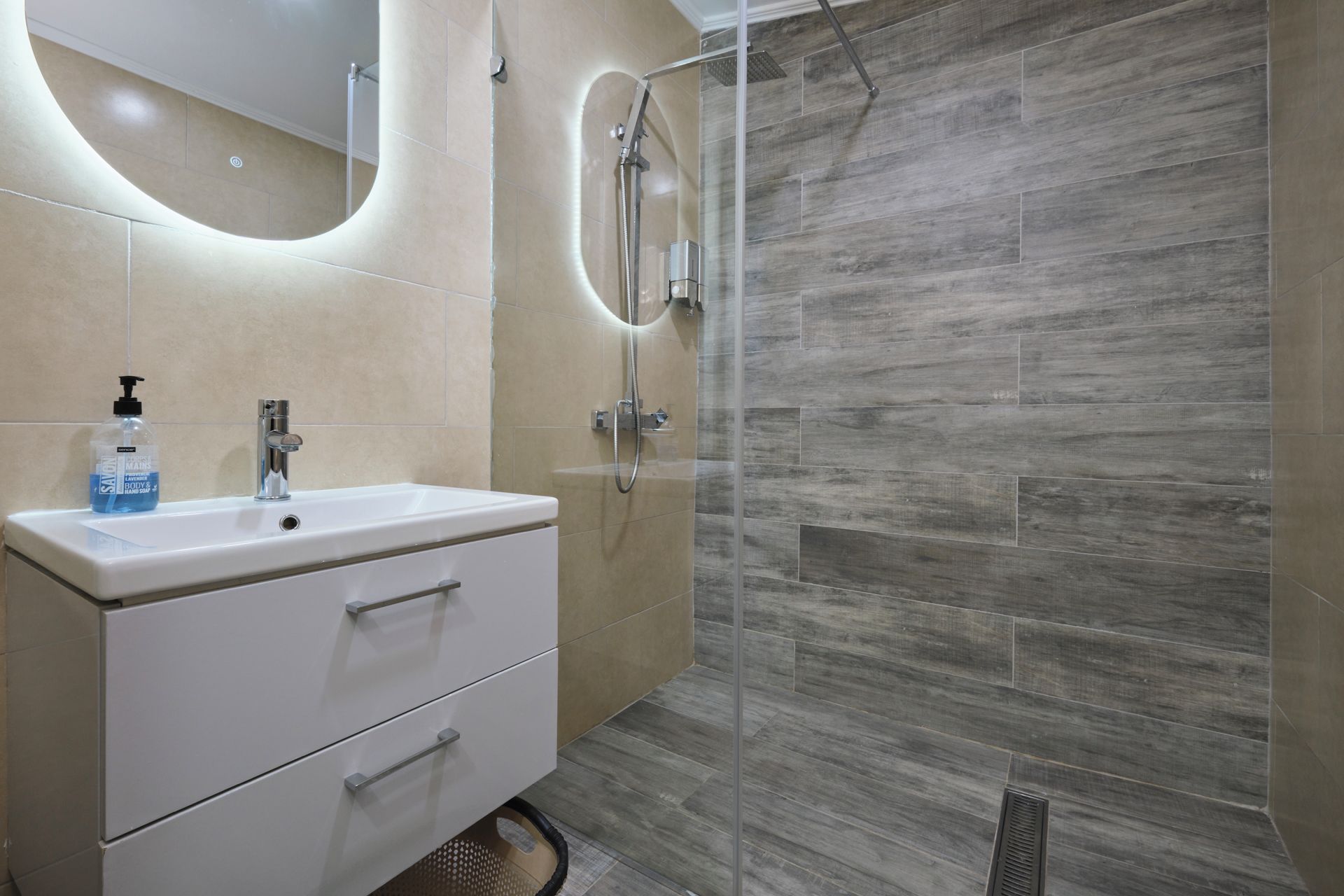 A modern bathroom with a white vanity, a glass shower enclosure, and beige tiles.