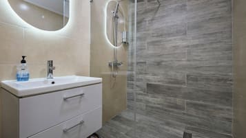 A modern bathroom with a white vanity, a glass shower enclosure, and beige tiles.