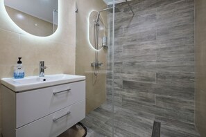 A modern bathroom with a white vanity, a glass shower enclosure, and beige tiles. - Studio 4 Luxurious, 3-minute walk to the beach in an exclusive neighborhood. (Oranjestad)