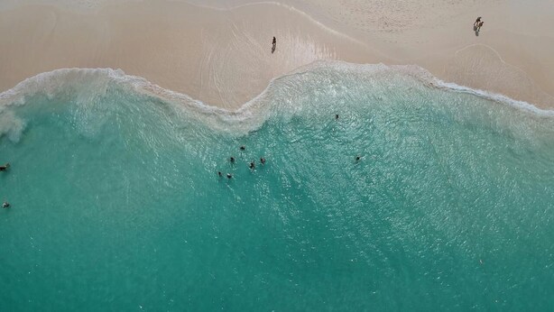 Vista aerea di una spiaggia con acque cristalline turchesi e una battigia sabbiosa.
