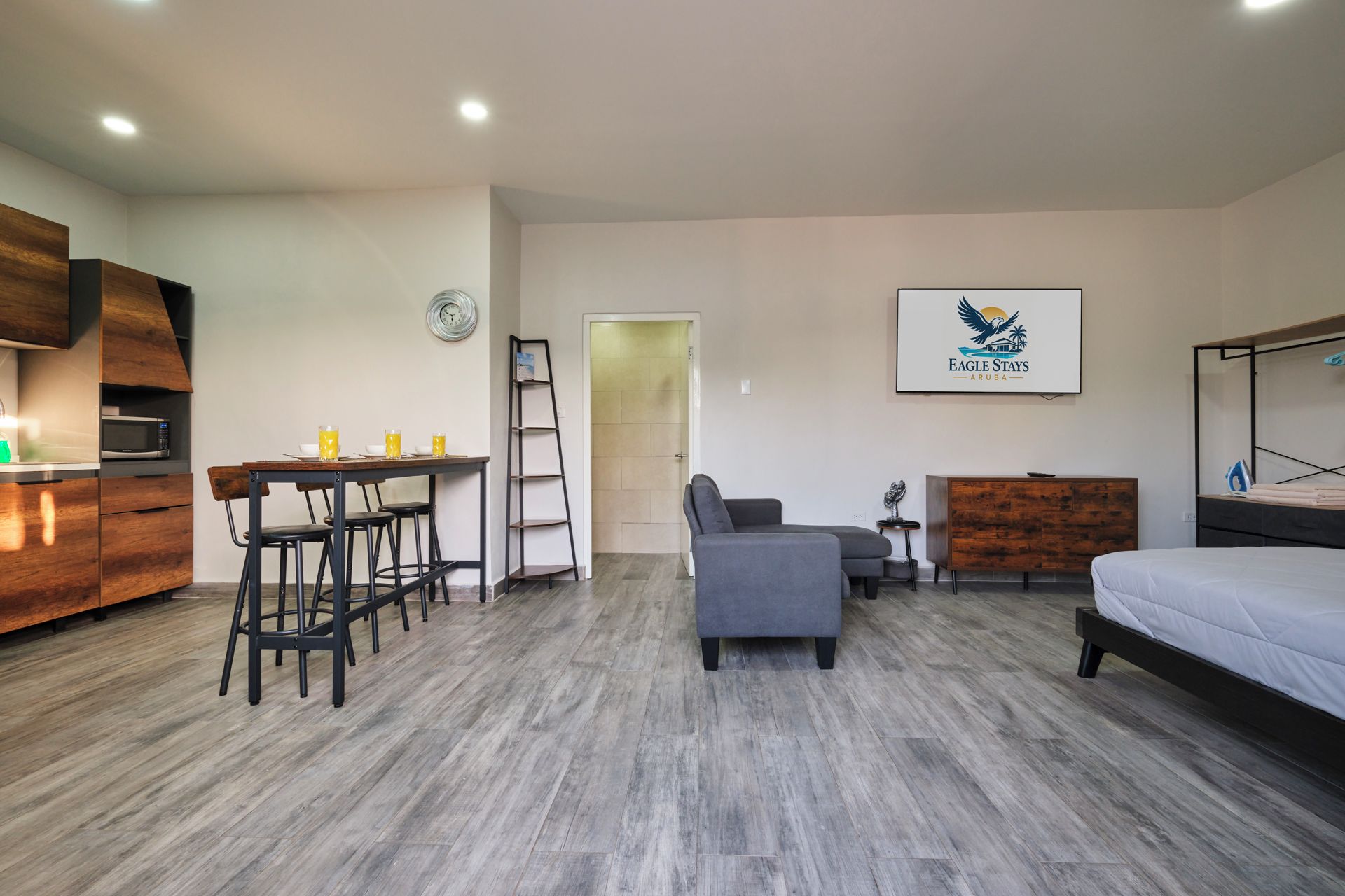 Habitación de hotel compacta con cama, escritorio con sillas, sofá, microondas y mueble de madera.