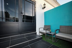 A modern outdoor seating area with a dark-colored door, a teal wall, and a small table with a chair. - Studio 4 Luxurious, 3-minute walk to the beach in an exclusive neighborhood. (Oranjestad)