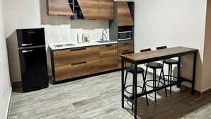 Una cucina compatta con forno a microonde integrato, macchina del caffè e frigorifero. È presente un tavolo da pranzo in legno con quattro sgabelli.