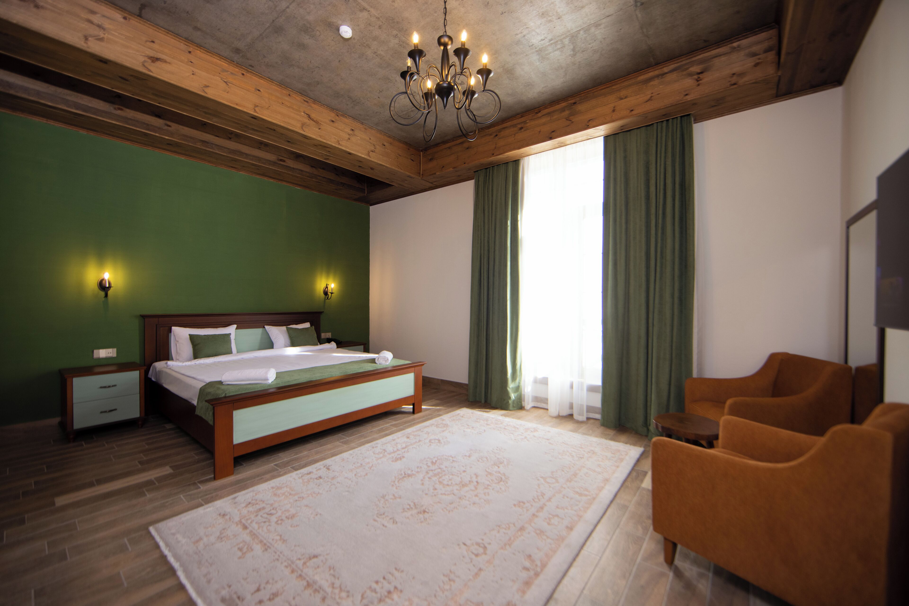 A bedroom with a wooden ceiling, a large bed, green curtains, and a chandelier.