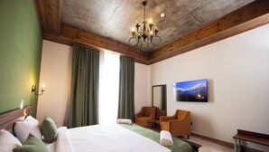 A hotel room with a large bed, a television mounted on the wall, a seating area with a chair and a small table, and a chandelier. - Xinali Hotel Xizi  (Altiagach)