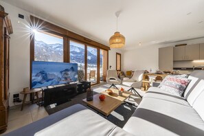 A modern living room with a large TV, comfortable seating, and a view of mountains.