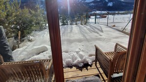 Una terrassa de fusta amb cadires, un paisatge nevós i muntanyes al fons.