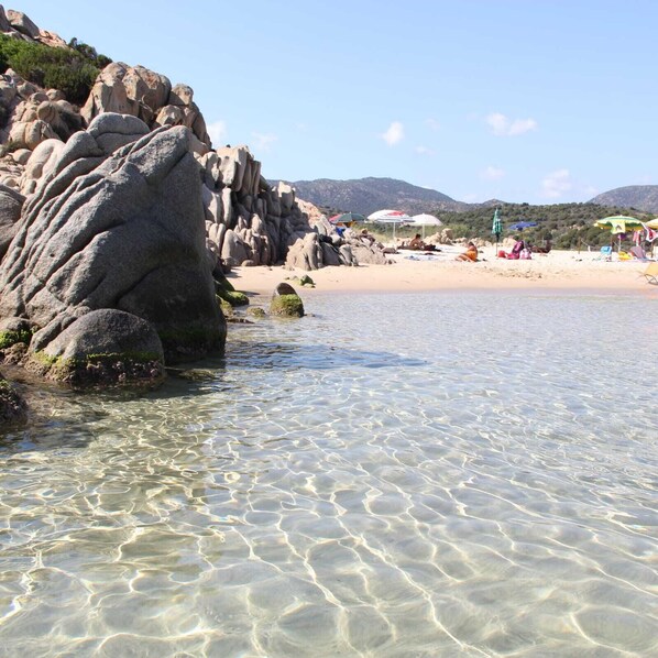 Wade into the calm waters of this serene beach, surrounded by large boulders and scenic mountain views.