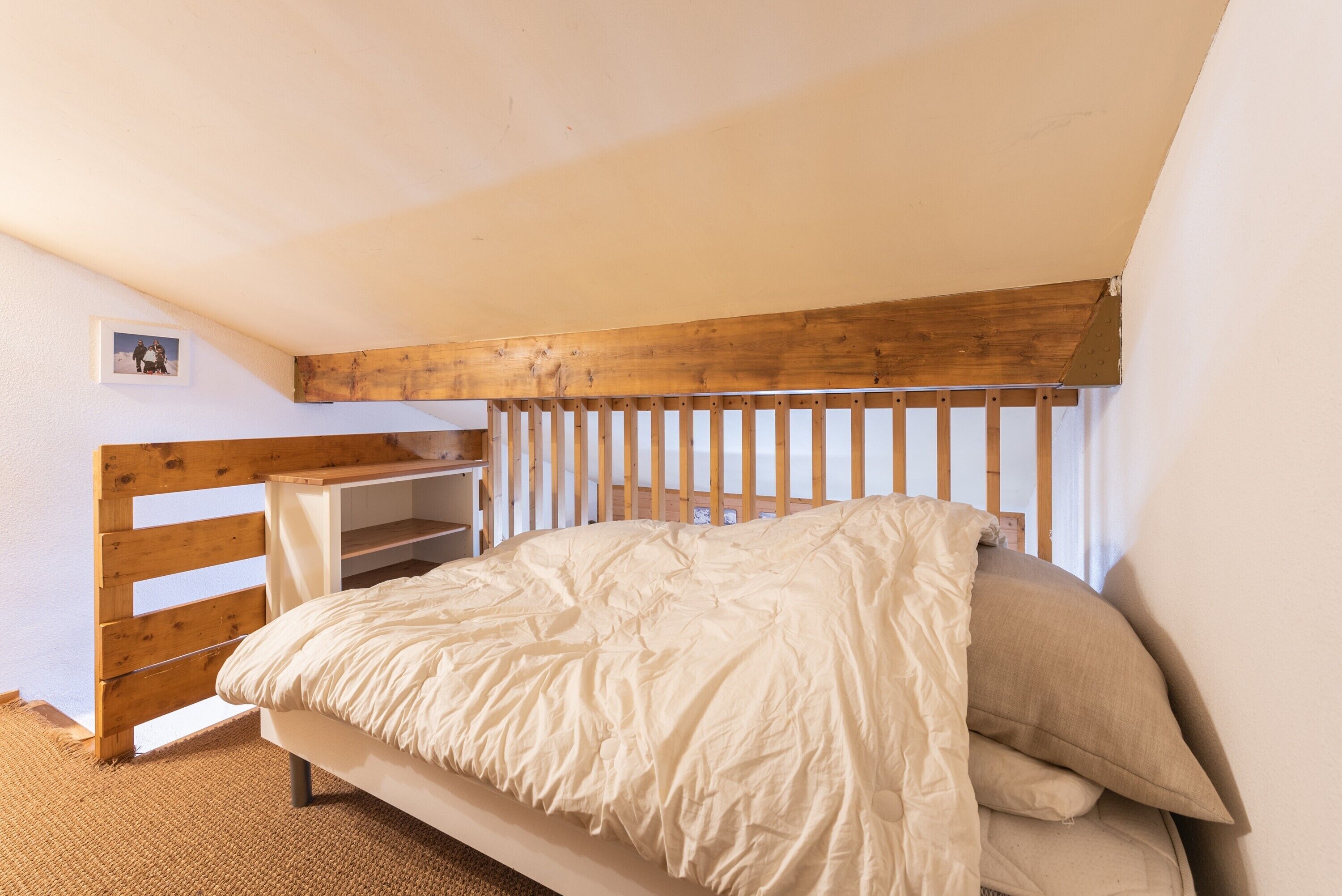 A bedroom with a wooden bunk bed, a white wall, and a small shelf.