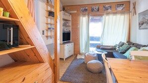 A cozy room with a wooden staircase, a television, a sofa, and a dining table.