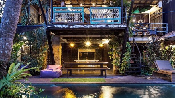 A modern building with a pool, outdoor seating, and a staircase leading to an upper level. - Singing River Front Villa (Tabanan)