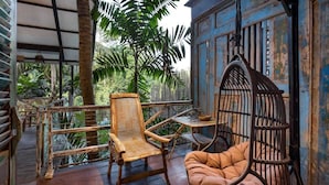 A wooden deck with a wicker chair and a hanging chair, surrounded by lush greenery. - Singing River Front Villa (Tabanan)